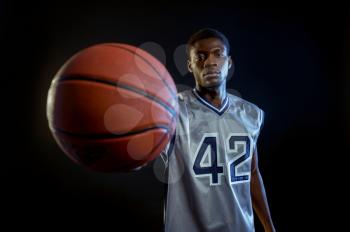 Basketball player shows a ball in studio, black background. Professional male baller in sportswear playing sport game, tall sportsman
