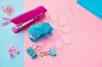 Stapler and paper clips closeup, blue and pink background. Office stationery supplies, school accessories