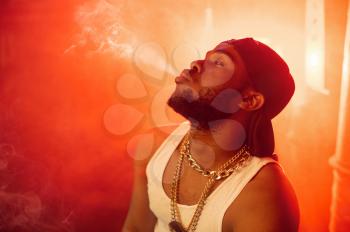Stylish rapper exhales smoke in studio with cool underground decoration. Hip-hop performer, rap singer, break-dance
