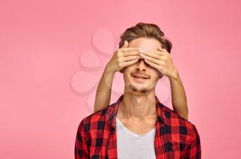 Young man with hands on his eyes, pink background, emotion. Face expression, male person looking on camera in studio, emotional concept, feelings