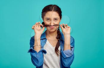 Funny young woman shows a mustache, blue background, positive emotion. Face expression, female person looking on camera in studio, emotional concept, feelings