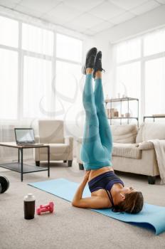 Girl doing exercise on the press, online fit training at the laptop. Female person in sportswear, internet sport workout, room interior on background