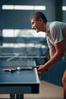 Man at the ping pong table, side view, male pingpong player. Sportsman playing table-tennis indoors, sport game with racket, active healthy lifestyle