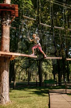 Little female climber leisures in rope park, playground. Child climbing on suspension bridge, extreme sport adventure on vacations, danger entertainment outdoors