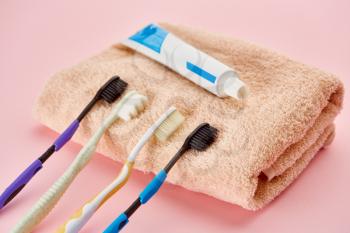 Oral care products, toothbrushes and toothpaste on towel, pink background, nobody. Morning healthcare procedures concept