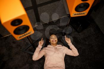 Happy woman lying on the floor and listens to music in speaker system store. Female person in audio shop, amplifier on background, buyer in multimedia salon