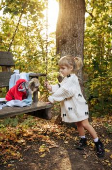 Kid play with funny dog on big wooden chair in the garden. Female child with puppy poses on backyard. Little girl and her pet having fun on playground outdoors, happy childhood