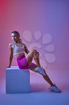 Sexy sportswoman poses at the cube in studio, neon background. Fitness woman at the photo shoot, sport concept, active lifestyle motivation