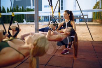 Women's group and instructor, exercise with ropes on sports ground, outdoors fitness training. Slim female athletes in sportswear, team fit workout, teamwork