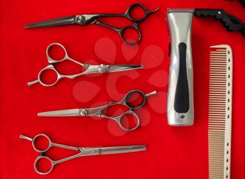 Hairdresser equipment, top view, red background hairdressing salon, nobody. Stylist tools, scissors, comb and electric hair clipper, hairsalon. Beauty business, professional service