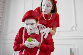 Two mime artists in red costumes, scene with apple. Pantomime theater, parody comedian, positive emotion, humour performance, funny face mimic and grimace