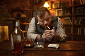 Man smokes cigarette and drinks alcohol beverage, bookshelf and rich office interior on background. Tobacco smoking culture