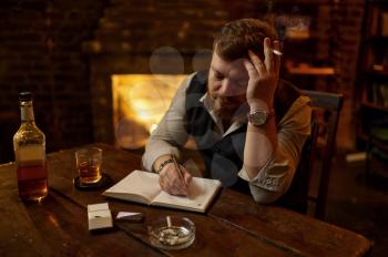 Man smokes cigarette and writes in notebook, wooden tabler on background. Tobacco smoking culture. Male smoker