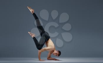 Male yoga keeps balanc in a difficult pose on hands, grey background. Strong man doing yogi exercise, asana training, top concentration, healthy lifestyle