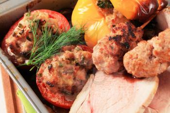Roast pork, minced meat kebabs and stuffed pepper and tomatoes in a baking pan