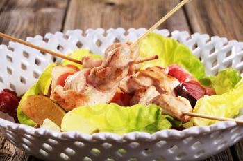 Chicken skewers and bacon served on lettuce leaves