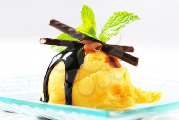 Scoop of yellow ice cream topped with chocolate sauce and mint sticks