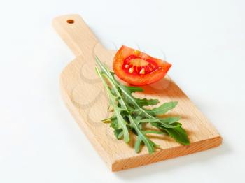 Rocket leaves and tomato wedge on cutting board