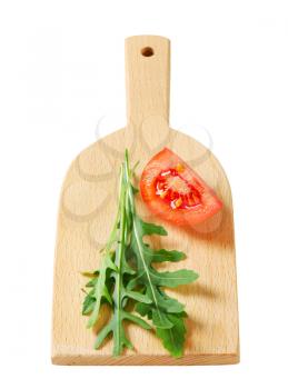 Rocket leaves and tomato wedge on cutting board