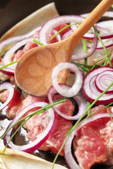 Raw pork, onion, and endive leaves on a frying pan