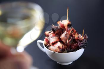 Bowl of bacon wrapped prunes and white wine