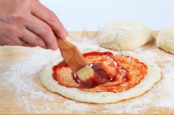 Cook spreading tomato sauce over pizza dough