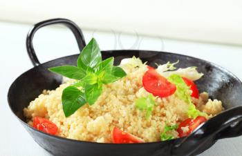 Couscous with salad greens and tomato in a pan