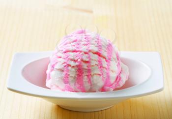Scoop of white pink ice cream in a dessert dish