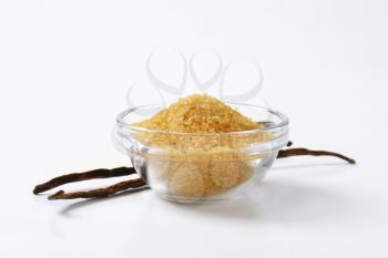 Bowl of golden brown raw cane sugar and two vanilla pods