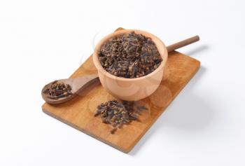 Heaps of dried cloves in a bowl, on wooden spoon and cutting board