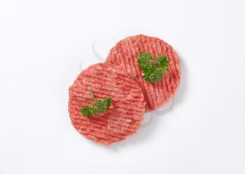 two raw hamburger patties with parsley on white background