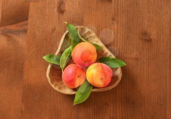 Three ripe apricots in wooden bowl