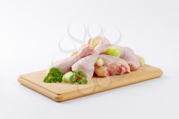 heap of raw chicken legs with onion and garlic on wooden cutting board