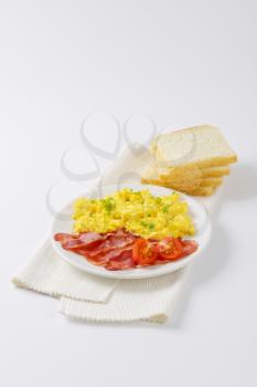 plate of scrambled eggs and pan fried bacon with slices of white bread on white place mat