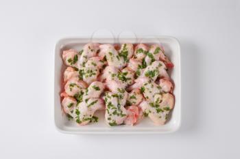 raw chicken wings with chopped parsley in white ceramic baking dish