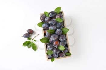 box of ripe plums on white background
