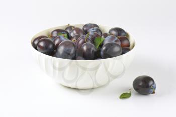 bowl of ripe plums on white background