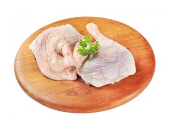 Raw chicken legs on round wooden cutting board