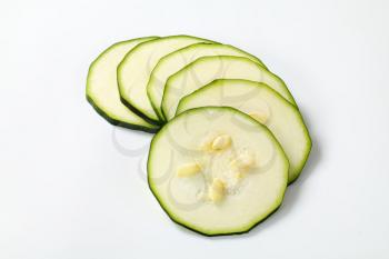 six thin slices of fresh zucchini on a white background