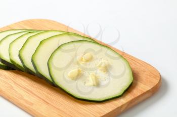 six thin slices of fresh zucchini on a wooden cutting board