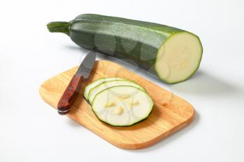 sliced fresh zucchini with a knife on a wooden cutting board
