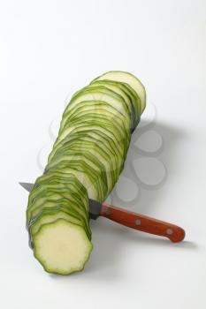 line of thin slices of fresh zucchini with a knife on a white background