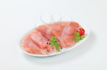 Raw turkey breast on plate, two slices cut off