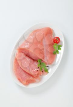Raw turkey breast on plate, two slices cut off