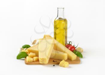 still life of parmesan cheese, vegetables and bottle of olive oil on white background