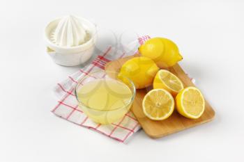bowl of freshly squeezed lemon juice, lemon squeezer and ripe lemons on wooden cutting board