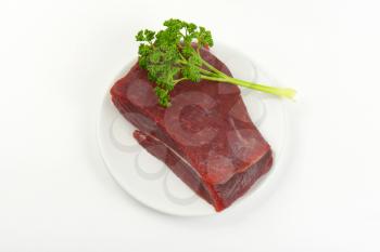 raw beef meat and fresh parsley on white plate