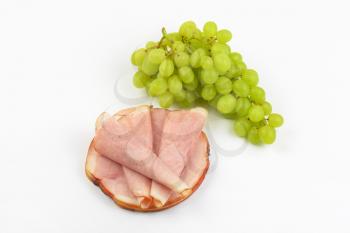 stack of ham slices and bunch of white grapes on white background