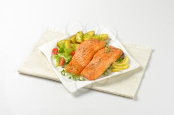 salmon fillets with roasted potatoes and vegetable garnish on square plate