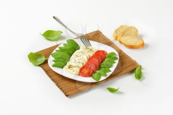 plate of fresh caprese salad on brown place mat and slices of bread roll